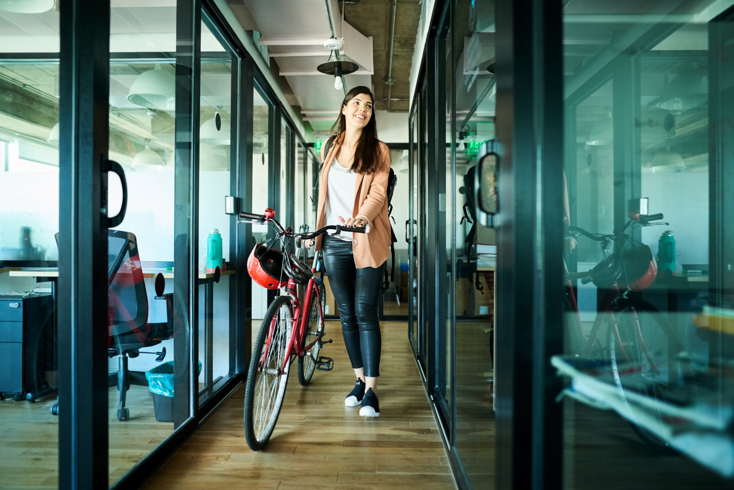 Young businesswoman pushing her bicycle and passing cubicles in the office